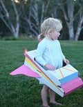 Child wearing a colorful cardboard airplane costume, playing outdoors.