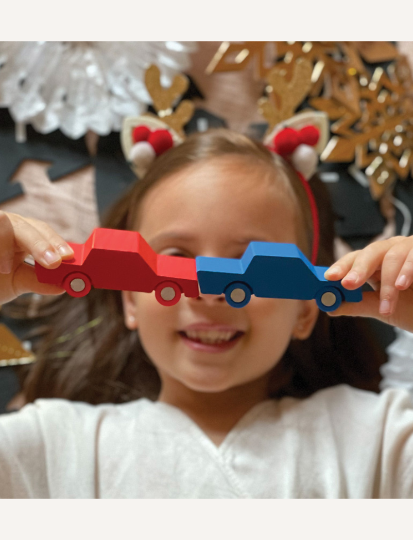 A child holds red and blue Way to Play wooden cars. Fun toy cars for road building and imaginative play.