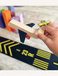 Child's hand holding a wooden airplane on a Way to Play airport runway with '23 R' marking. Airport play for kids.