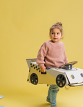 Young girl wearing a pink sweater holding a cardboard race car costume.