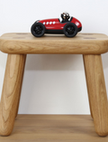 Red vintage toy race car with number 5 on a wooden stool in front of a white wall.