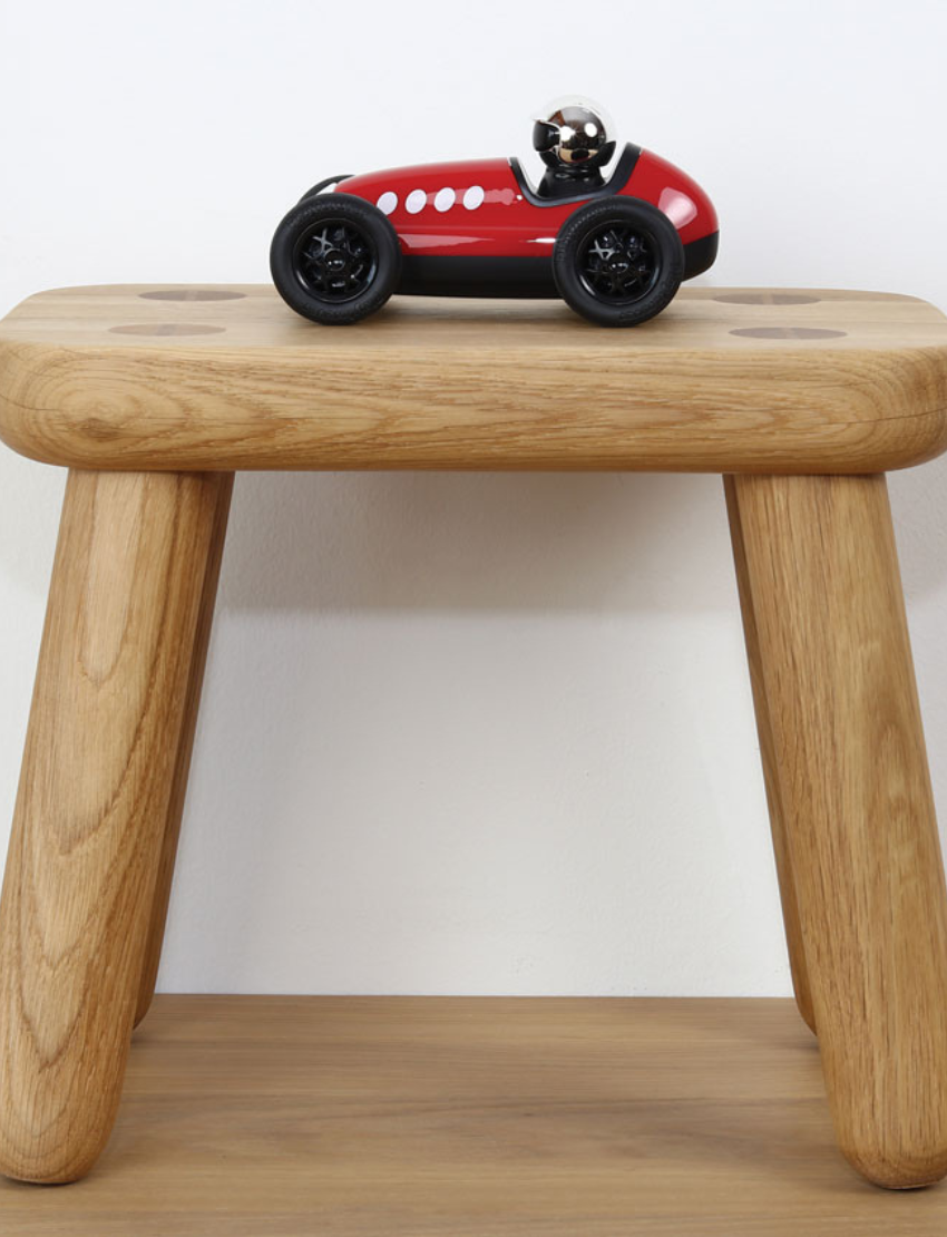 Red vintage toy race car with number 5 on a wooden stool in front of a white wall.