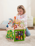 Toddler girl focused on playing with a wooden activity cube, bead maze, and gears.