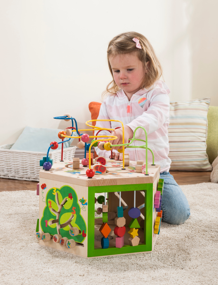 Toddler girl focused on playing with a wooden activity cube, bead maze, and gears.