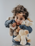 Close-up of a young child with curly hair hugging multiple plush animals.