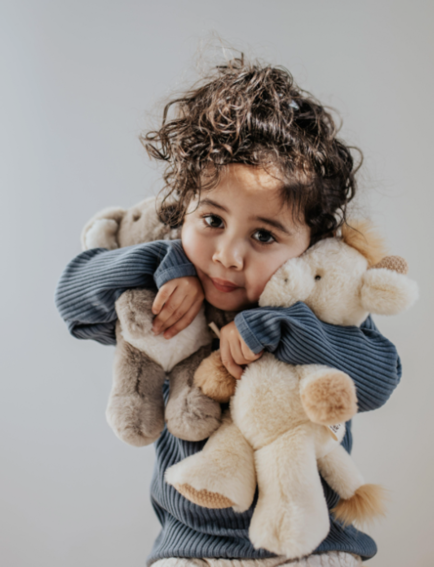 Close-up of a young child with curly hair hugging multiple plush animals.
