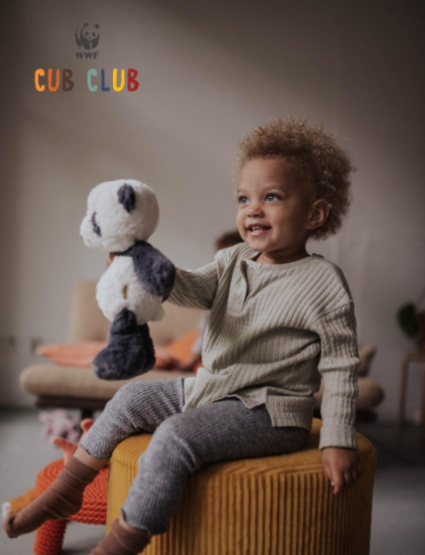 Smiling toddler sitting on a yellow ottoman holding a plush panda, with 'WWF CUB CLUB' logo.