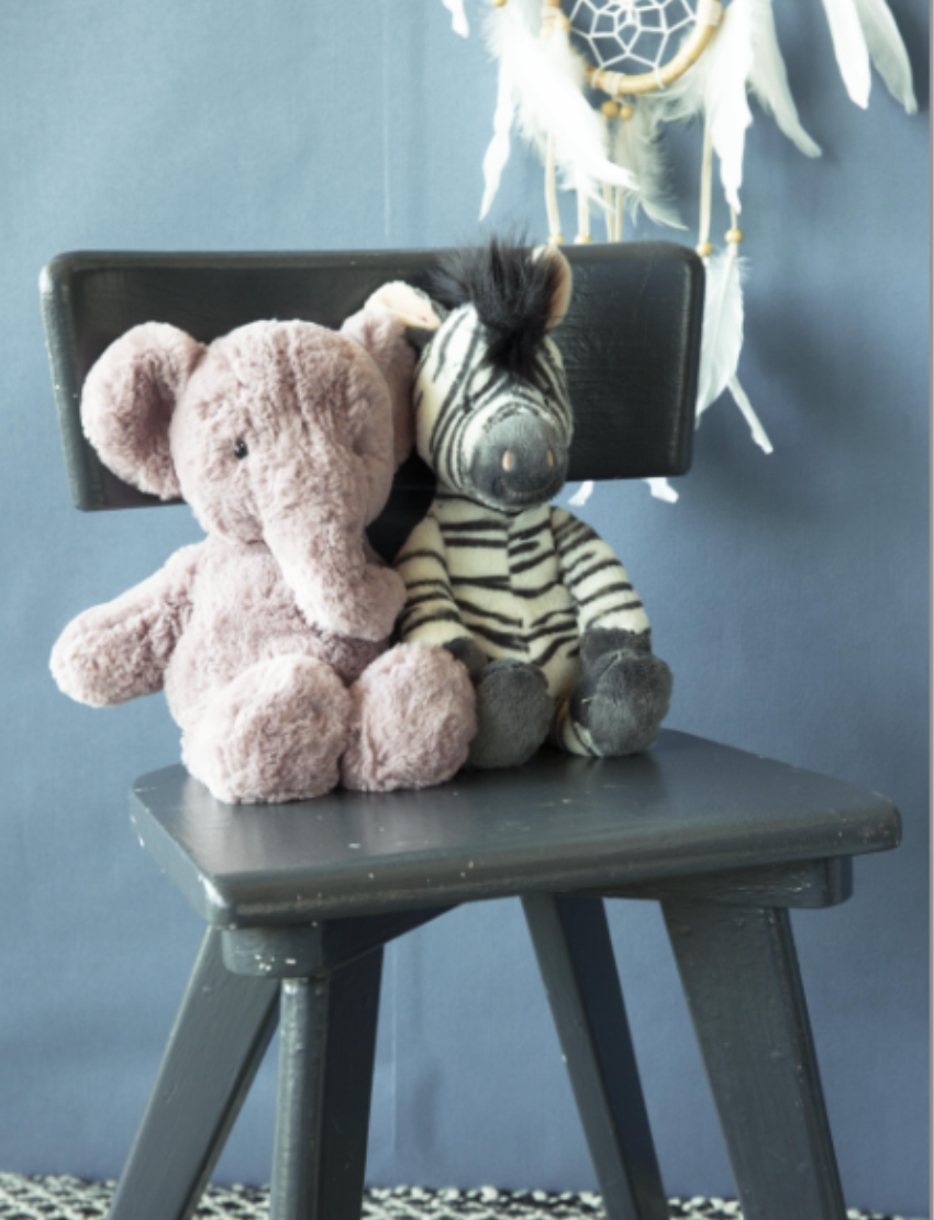 Plush elephant and zebra sitting on a dark grey chair in front of a blue wall with a dreamcatcher.