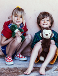 Young girl and boy smiling outdoors, holding plush animals; girl holds a green dinosaur, boy holds a monkey.