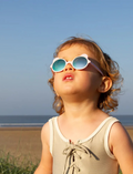 Close-up of a toddler with light brown curly hair wearing pink bear-shaped sunglasses.