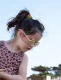 Young girl with dark hair in a ponytail wearing pink bear-shaped sunglasses.