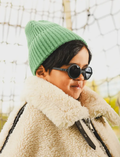 Young boy with dark hair wearing black round Ki ET LA sunglasses and a green beanie, with a shearling jacket.