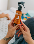 Hands holding Melo Magnesium Spray bottle, ready for application.