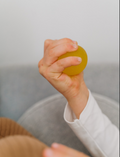 A child's hand squeezes The Play Way's yellow squishy ball, a therapist-designed tool for sensory soothing.