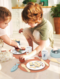 Two children enjoying a wooden dining playset, setting the table and engaging in pretend mealtime fun.