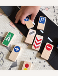Child playing with wooden toy road signs and a road mat, including stop and parking signs.
