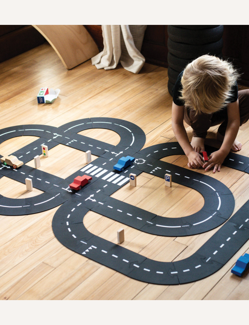 Child playing with a Waytoplay road set on a wooden floor, creating a race track.