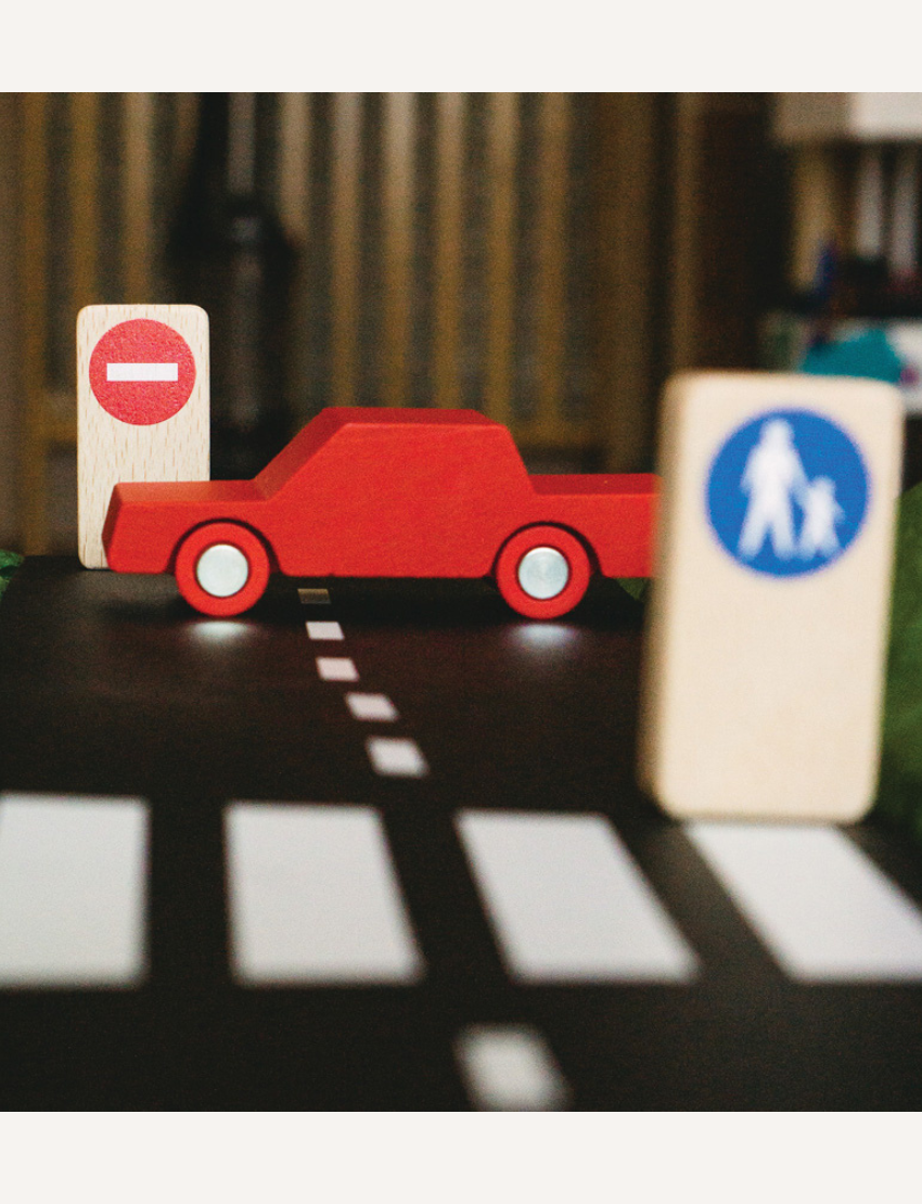 Close-up of a red toy car on a toy road with traffic signs and a crosswalk.