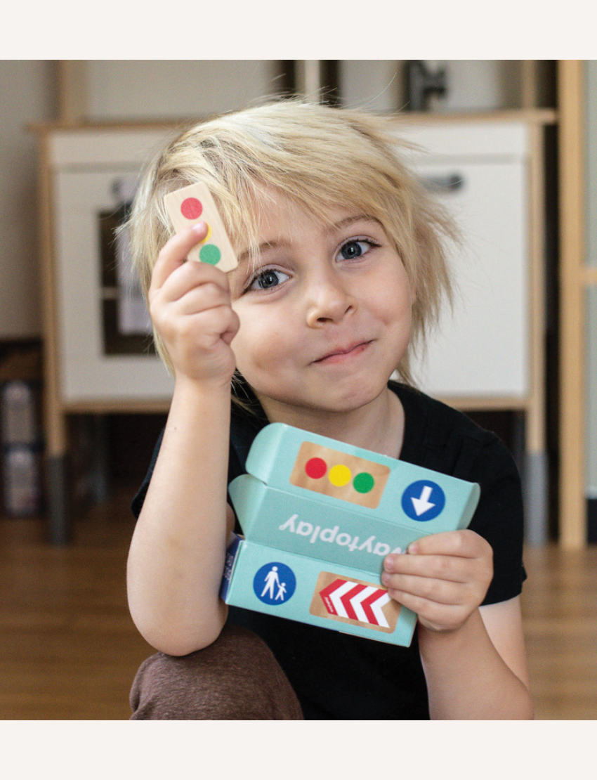 Happy child holding Waytoplay toy road signs, including traffic light and arrows.