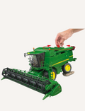 Child's hand adjusting the header on a green John Deere combine harvester.