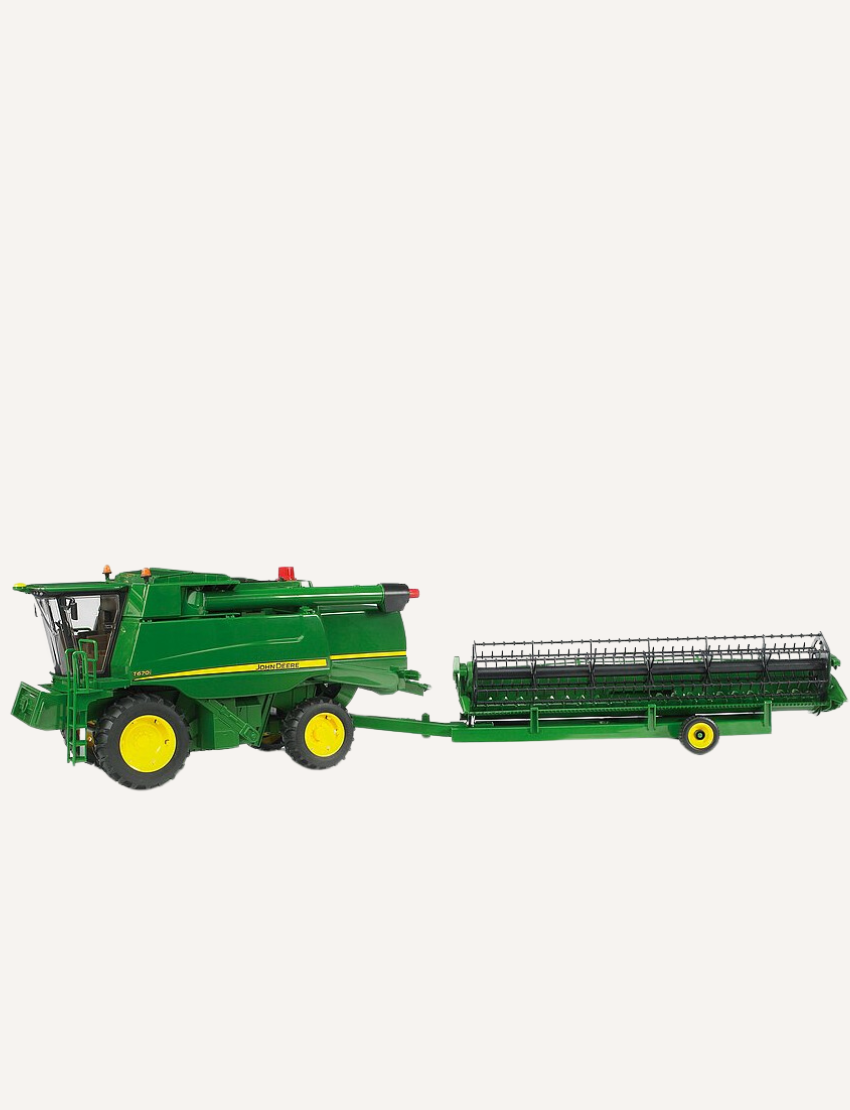 Green John Deere combine harvester towing a detachable green header on a trailer.