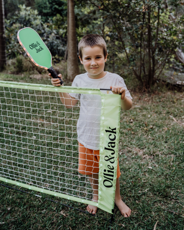 Boy holding a glowing paddle tennis racket by a net in a garden