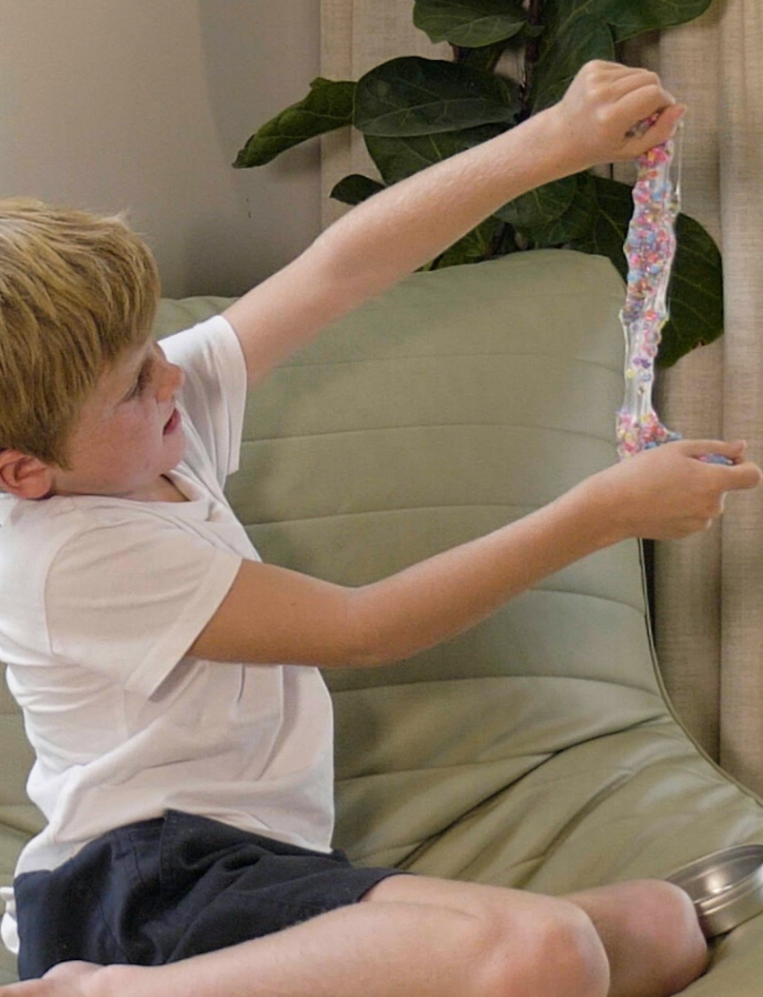 A child stretching colourful Crazy Aaron's Thinking Putty from The Play Way's therapist-designed regulation kit.