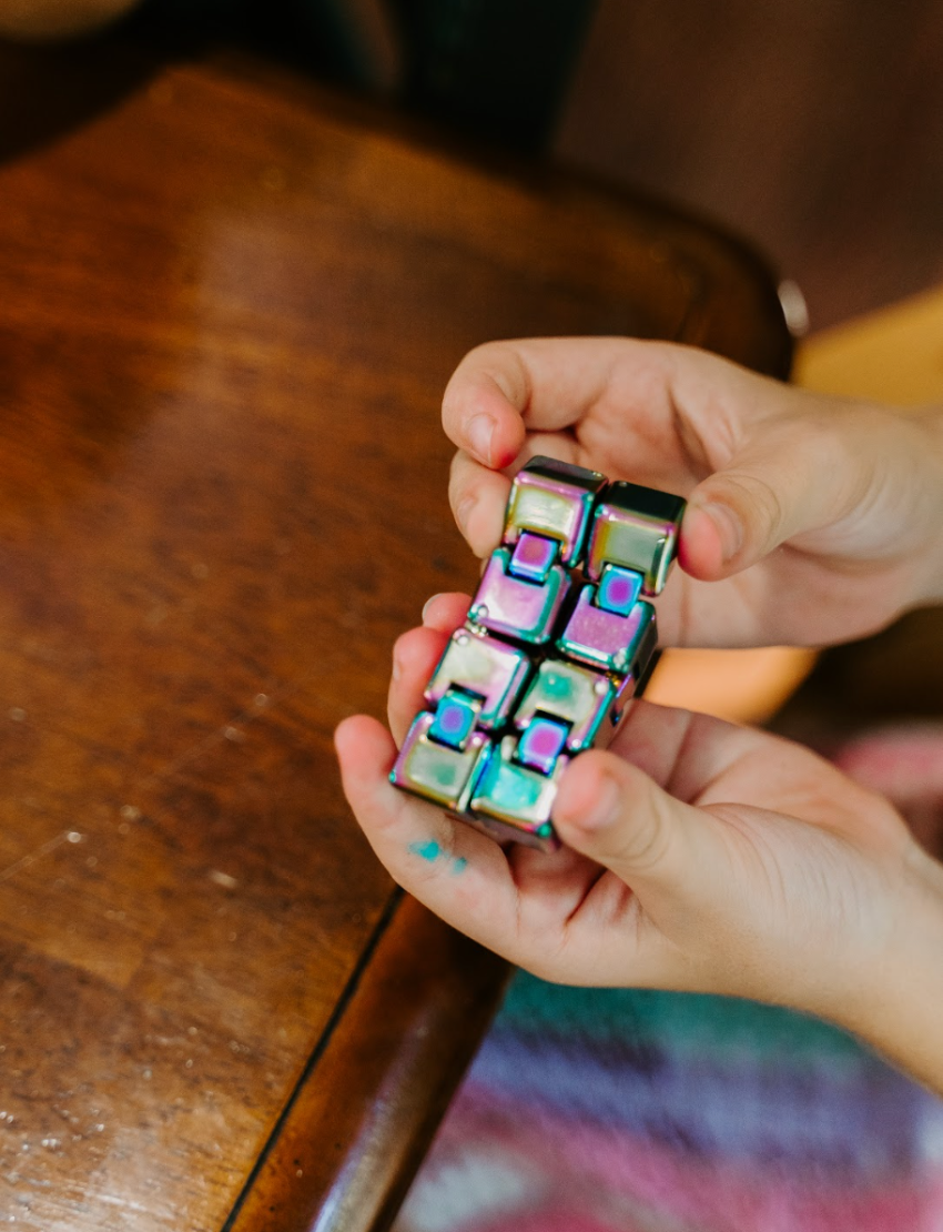 Child's hands manipulate a colourful Infinity Cube, a fidget tool from The Play Way Regulation Preferences Kit for focus.