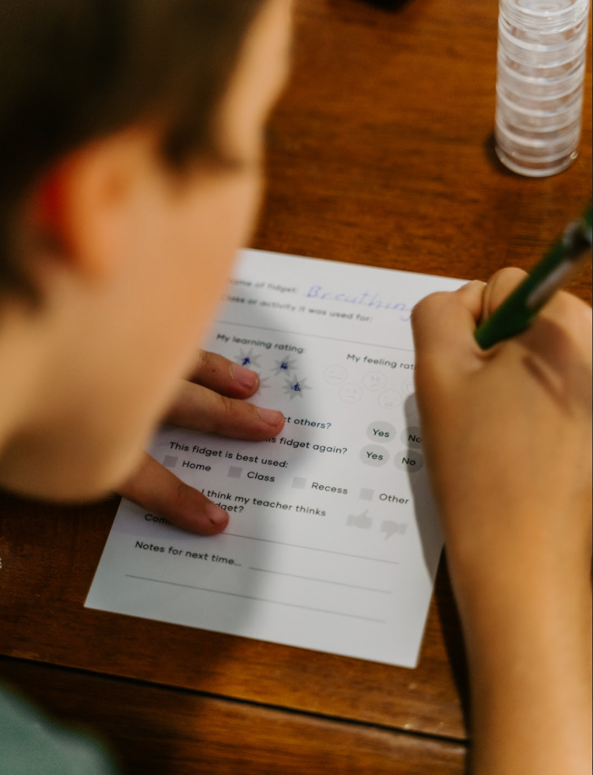 Overhead view of hands using a green pen to complete a worksheet from The Play Way's Reflection Kit for emotional regulation and self-discovery.