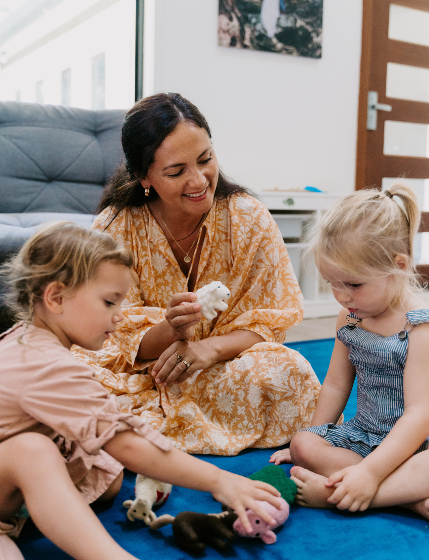 The Early Years Language Program by Therapy At Home features an open teal box neatly filled with educational toys, animal figurines, wooden blocks, a toy tea set, illustrated cards, books, and activity sheets for play-based learning and language development.