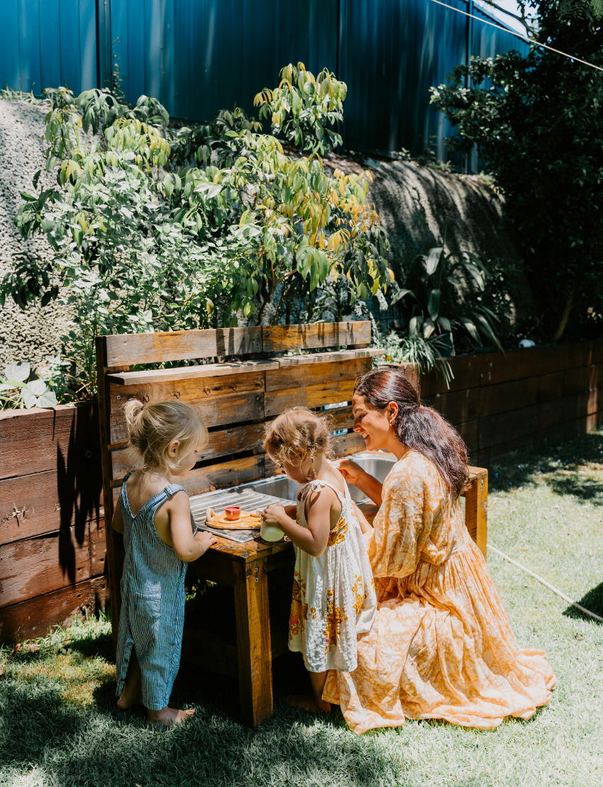 The Early Years Language Program by Therapy At Home features an open teal box neatly filled with educational toys, animal figurines, wooden blocks, a toy tea set, illustrated cards, books, and activity sheets for play-based learning and language development.