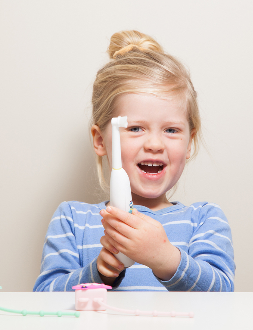 Happy blonde girl in blue striped shirt holding a white electric toothbrush.