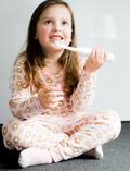 Young girl in pajamas smiling while holding a white electric toothbrush.