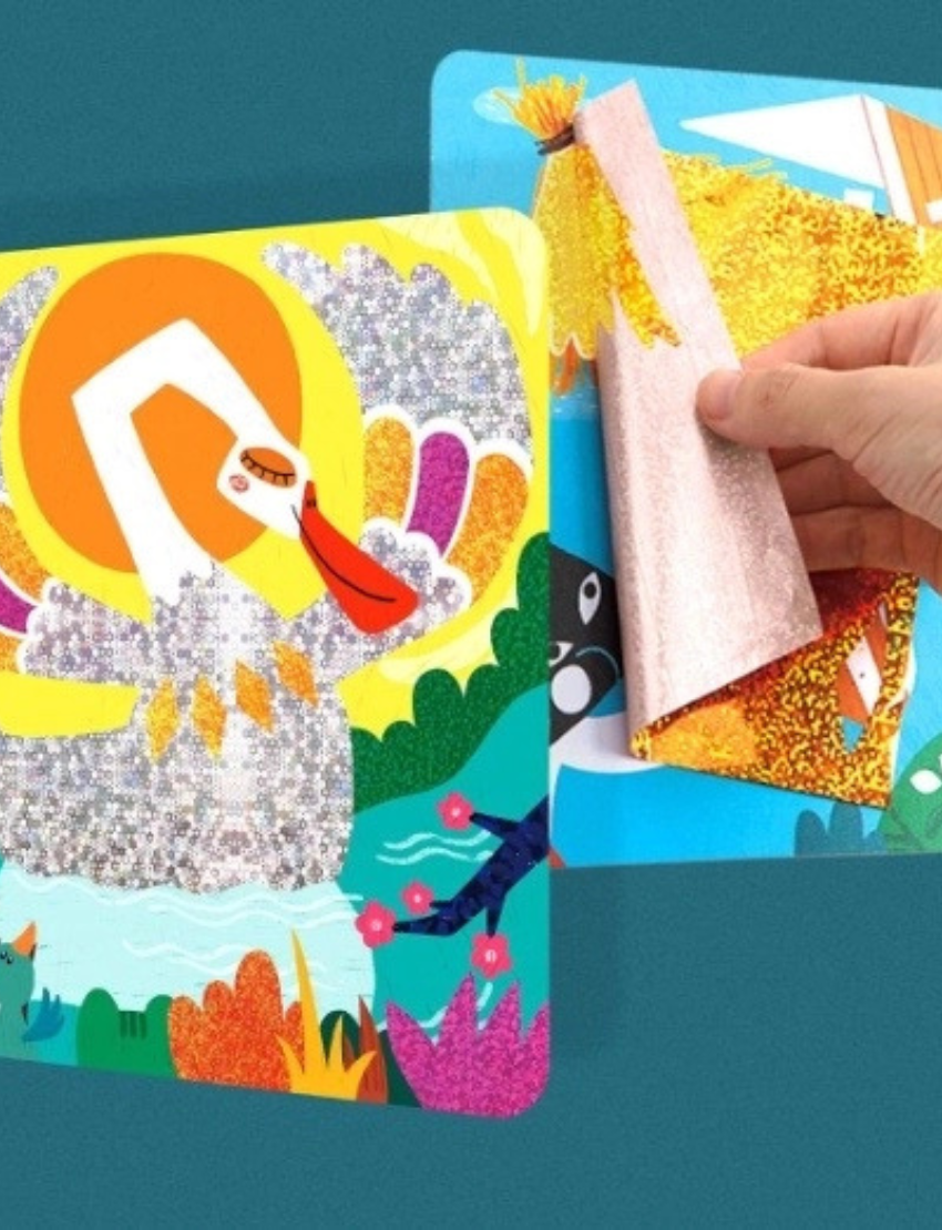 Close-up of a hand applying glitter stickers to create a swan artwork from 'Flash Stickers - The Ugly Duckling'.