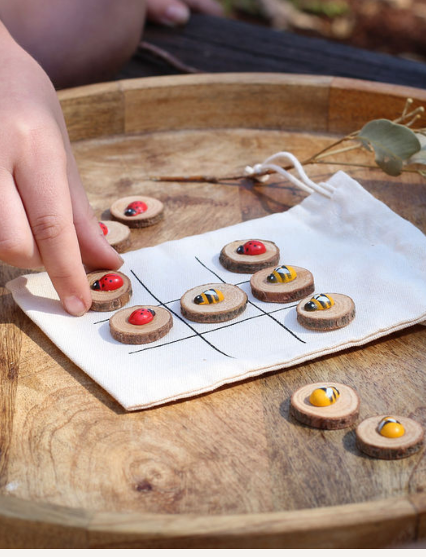 Poppy & Daisy DIY Tic-Tac-Toe kit with drawstring bag, wooden slices, charms, paint, and instructions.