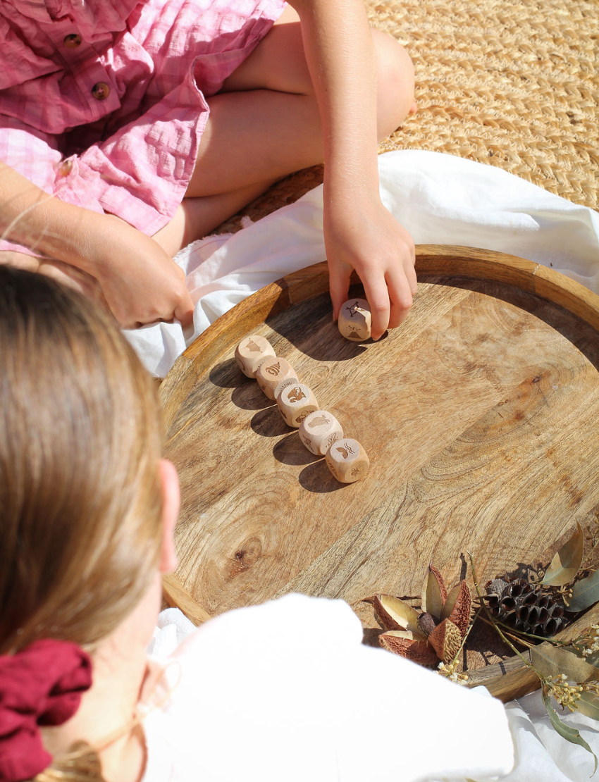 Children playing with Poppy & Daisy nature story cubes on a wooden tray outdoors.