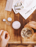 Hands assembling lavender lip balm kit on a wooden surface, showing ingredients, tin, and craft cup.