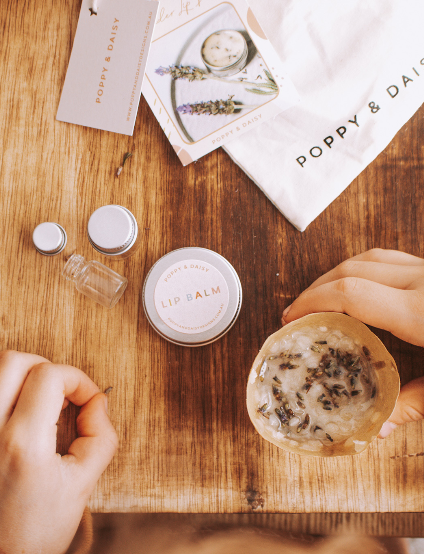 Hands assembling lavender lip balm kit on a wooden surface, showing ingredients, tin, and craft cup.