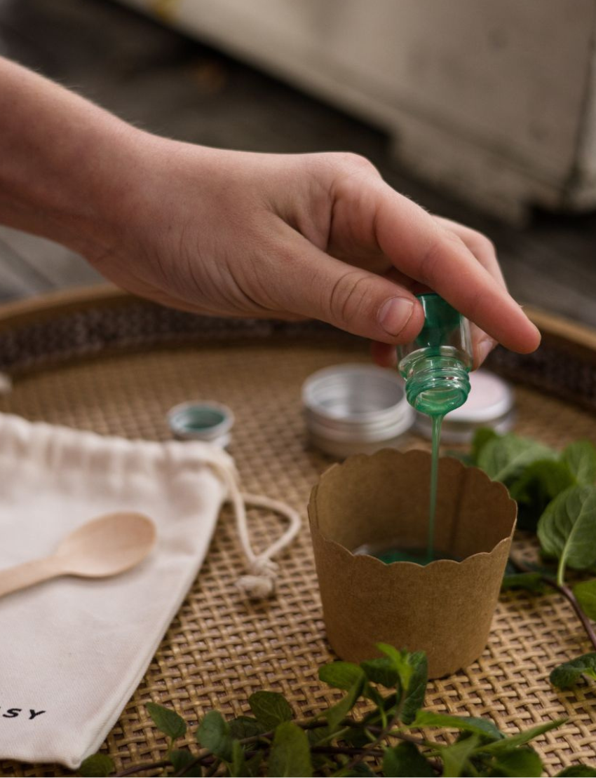 Poppy & Daisy DIY Peppermint Lip Balm kit: bag, balm tin, green liquid, wooden spoon, and cup.