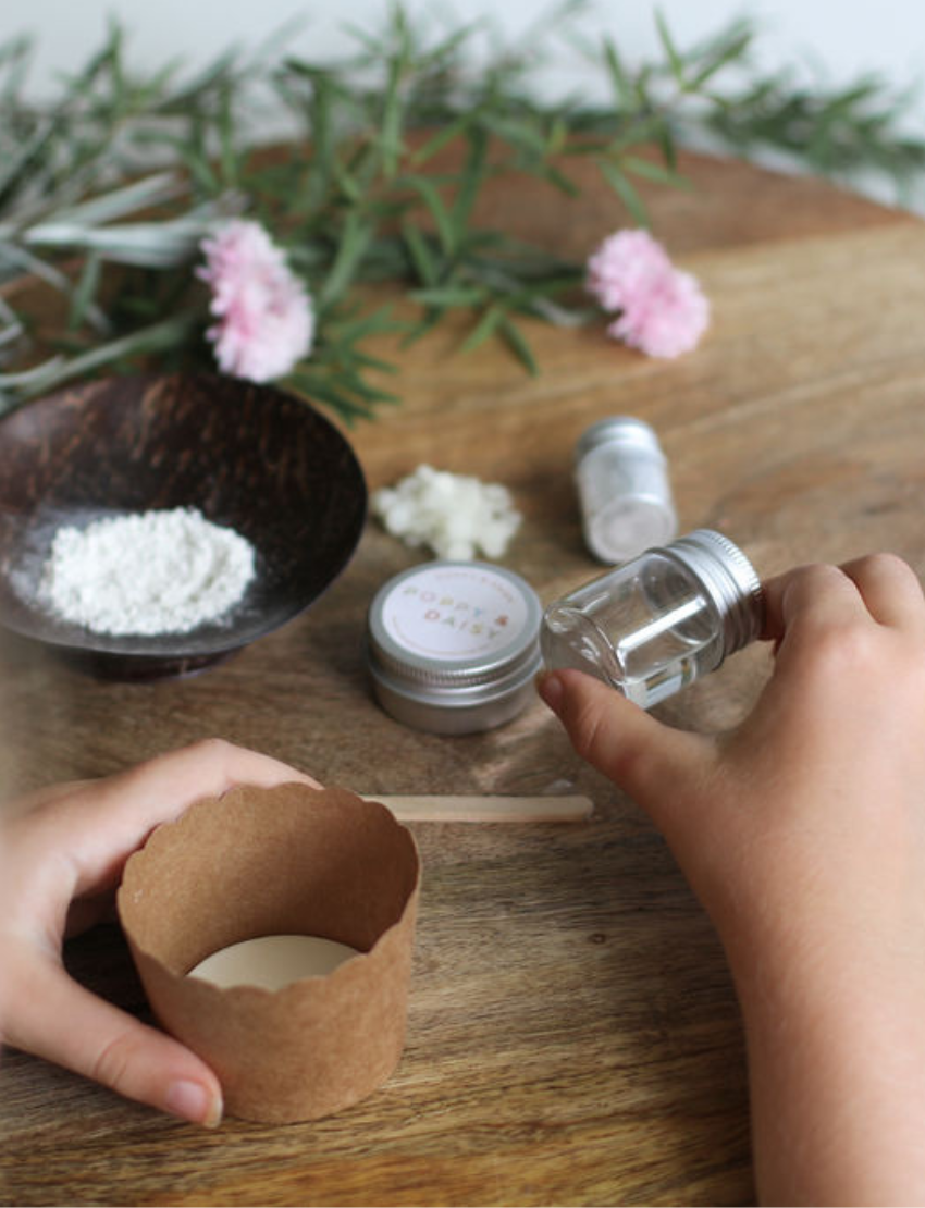 Hands mixing glitter and powder in a paper cup, with a tin and small bottles of Poppy & Daisy body glitter.