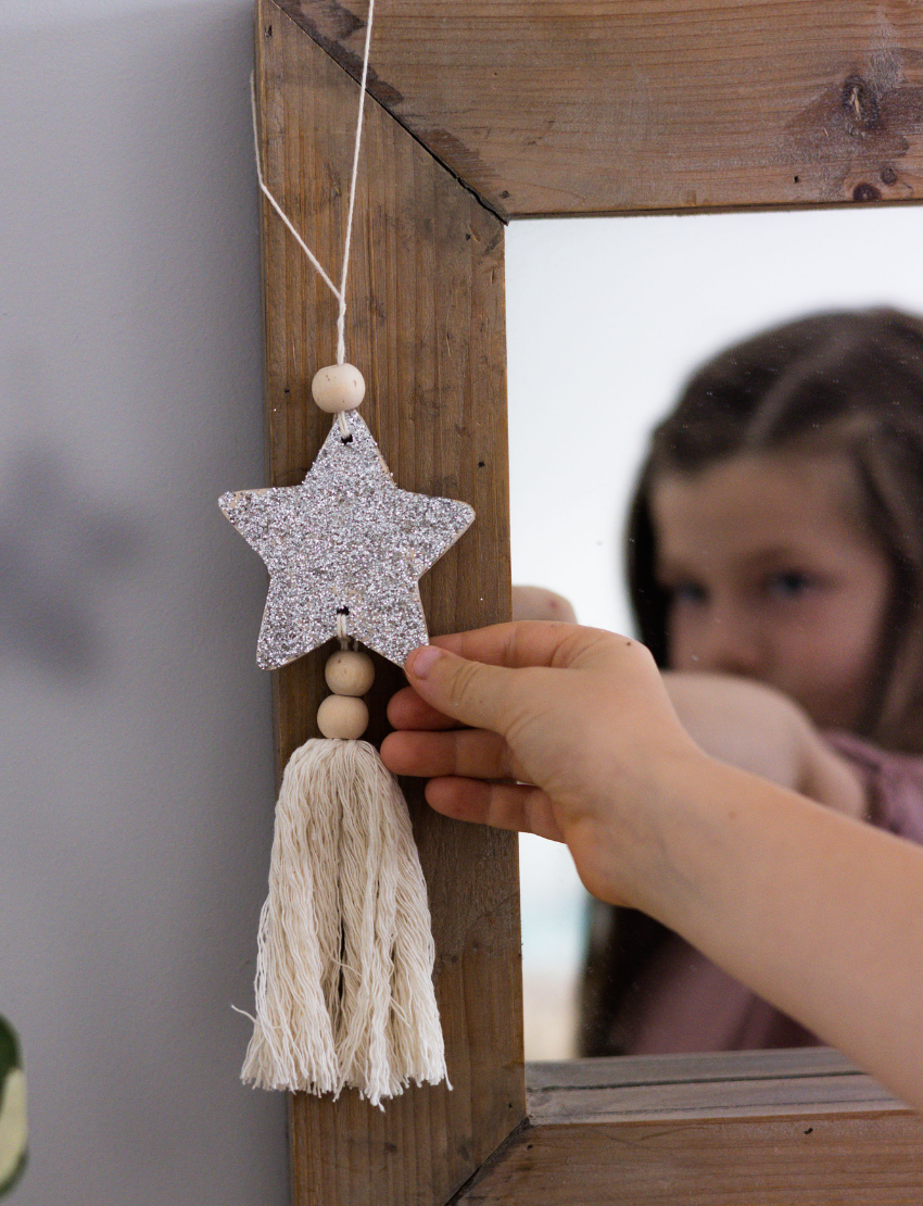 Girl's hand holding a glitter star decoration with beads and a tassel, reflected in a mirror.