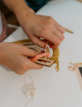 Close-up of hands weaving pink yarn onto a wooden frame for a macrame rainbow craft project.