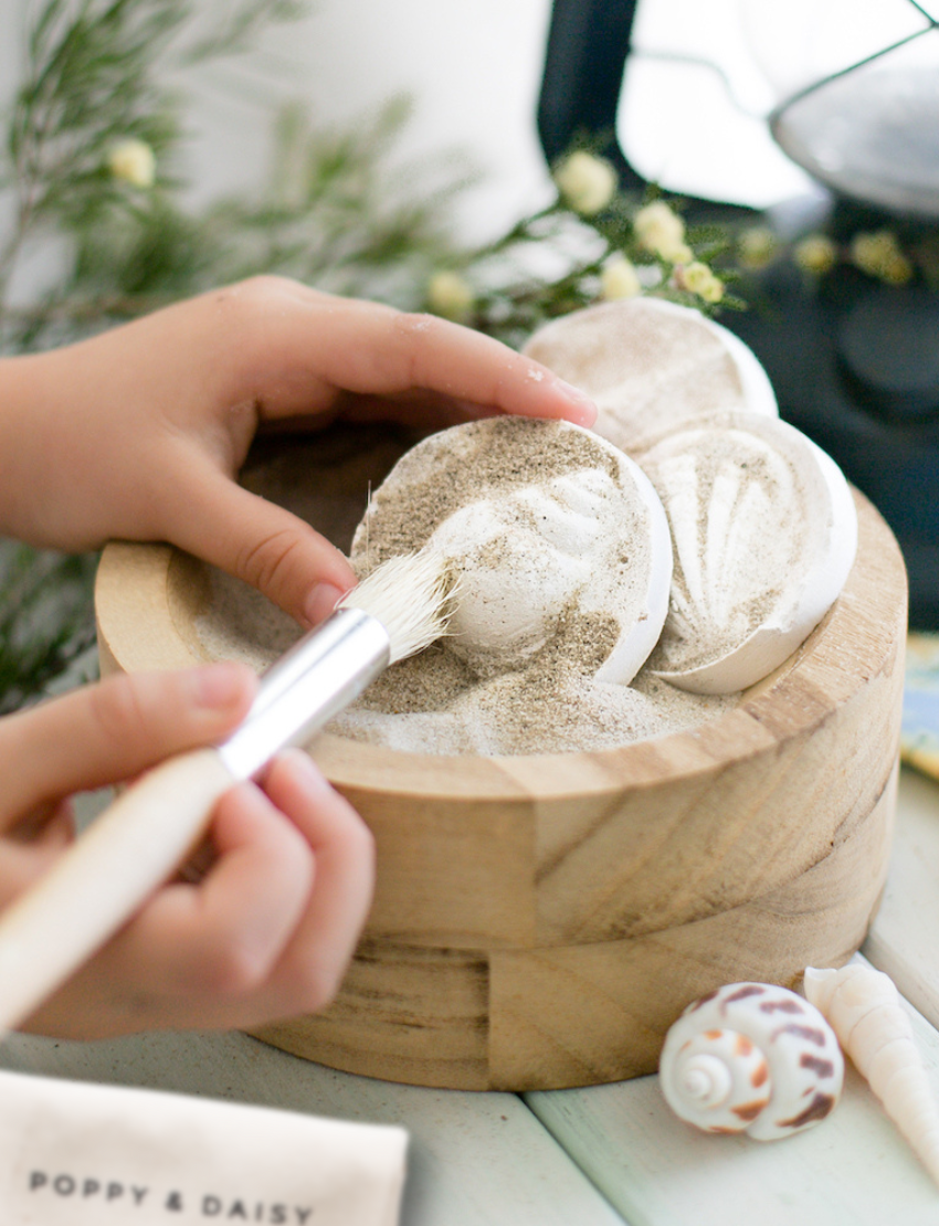 The Play Way 'Let's Create Fun Fossils' DIY kit components: sand, plaster, shells, and tools for unearthing ancient treasures.
