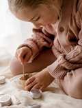 Close up of young girl's hands mixing mineral makeup in a paper cup with a wooden stick.