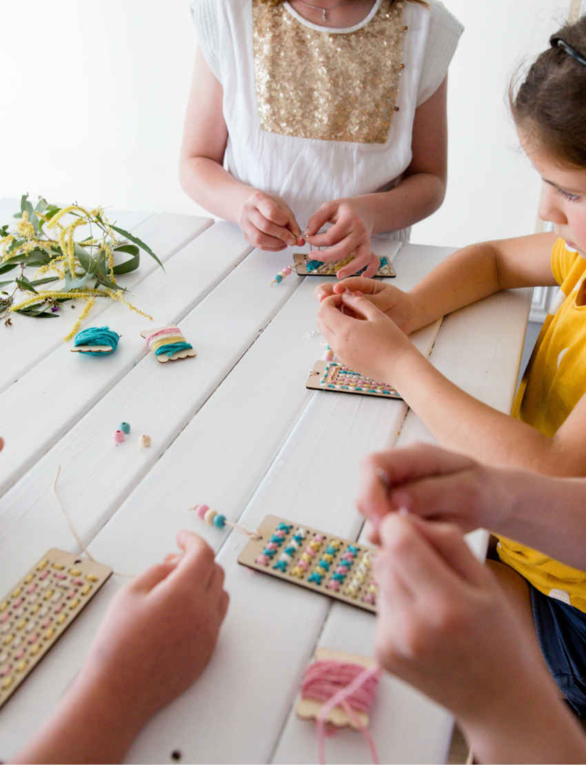 Children's hands busy creating DIY embroidered bookmarks with colorful yarn and wooden boards.