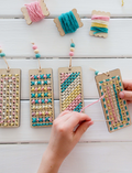 Close-up of four completed DIY embroidered bookmarks, showcasing colorful stitches and wooden beads.
