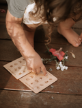 Child's hands pointing at Poppy & Daisy Nature Hunt cards with nature illustrations on wooden boards.