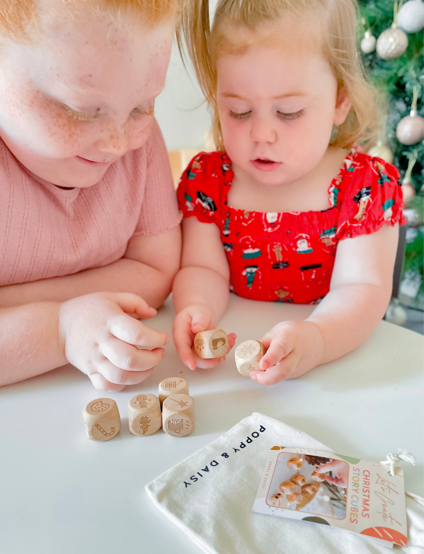 Two children focused on playing with Christmas story cubes from a DIY kit on a white table.