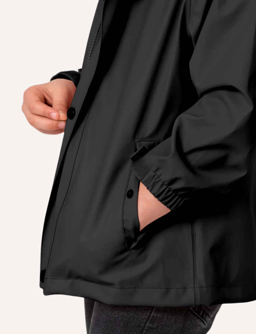 Close-up of a black kids' rain jacket, showing hands fastening a pocket with a button and elastic cuff detail.