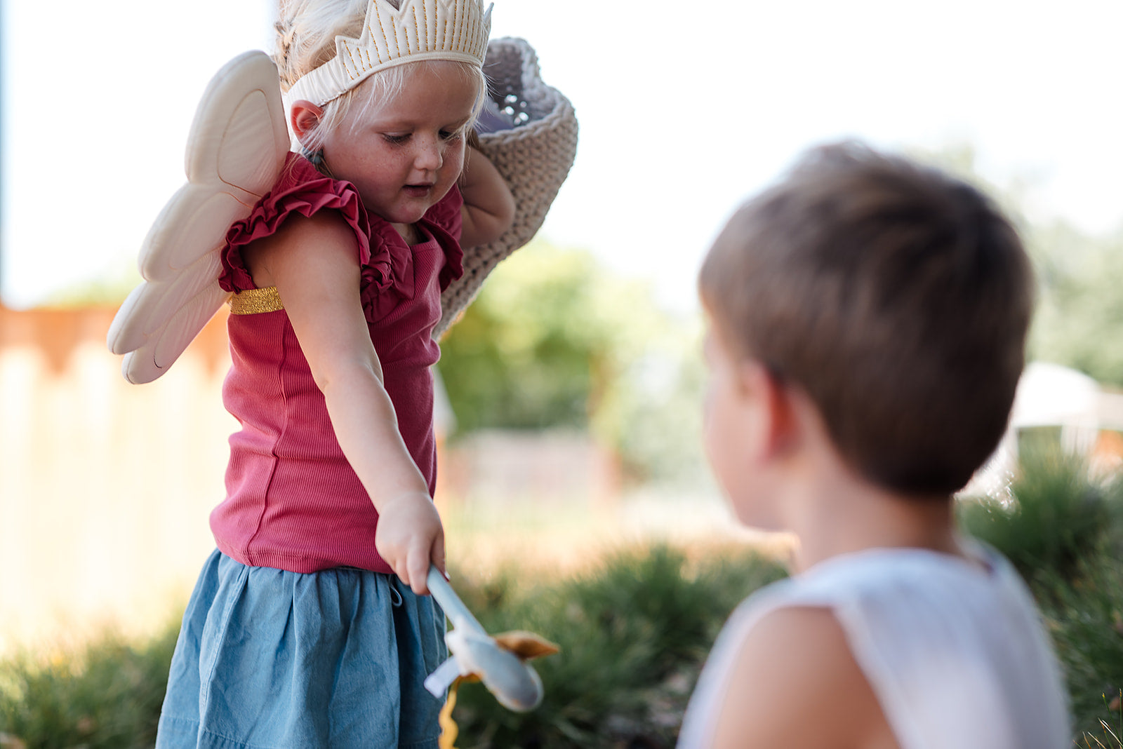 Child in a fairy costume interacting with another child outdoors.